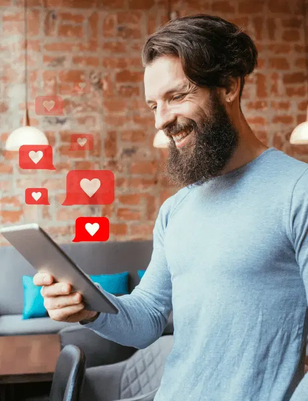 Man smiling at a tablet, with red heart notifications floating nearby in a cozy brick-walled room, appreciating the seamless experience of managed hosting.