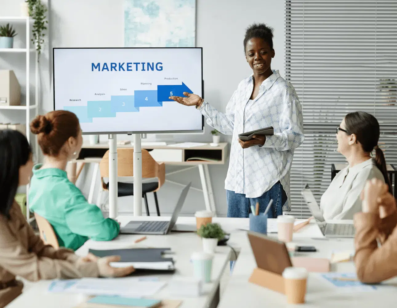 A person presents a marketing strategy on a screen to a group seated at a table with laptops and notebooks, highlighting the benefits of managed web hosting for seamless integration with WordPress.