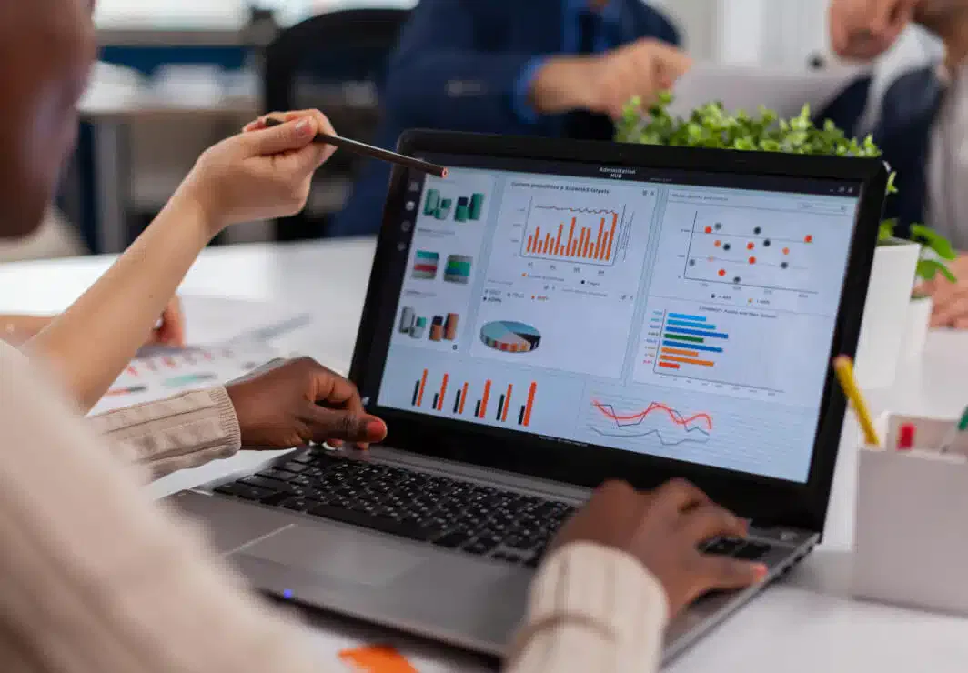 In an office setting, a person points at data charts on a laptop screen, illustrating various graphs and statistics related to managed hosting solutions.